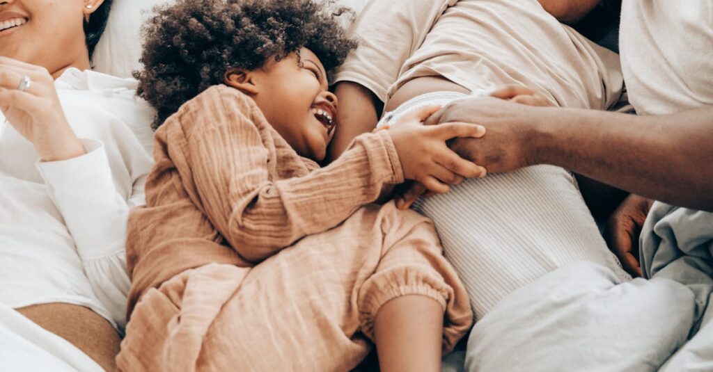 From above of smiling ethnic kids playing with father while resting together on bed lying near mother