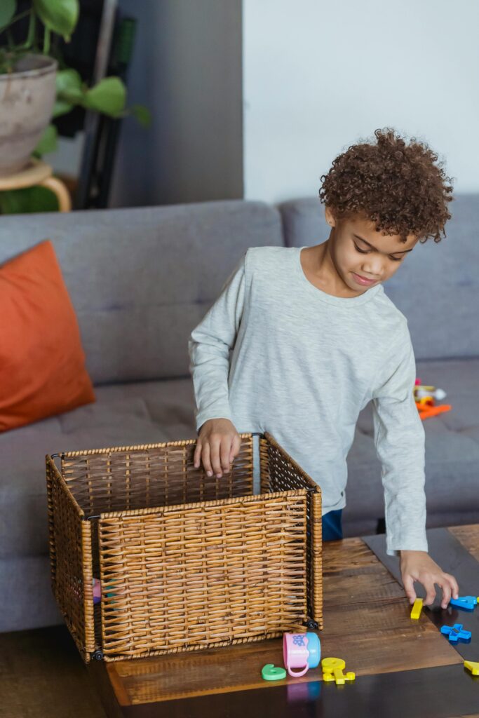 Young boy with curly hair playing with toys and basket on coffee table in cozy living room.