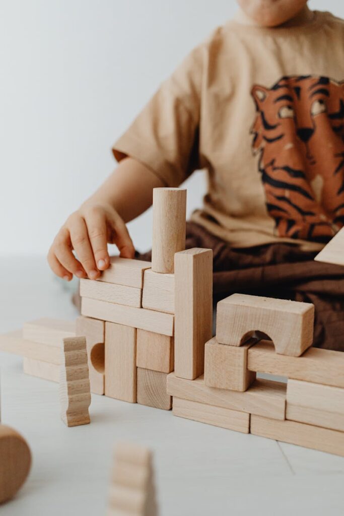 A child playing with wooden building blocks in an indoor playroom setting, focused on creativity.